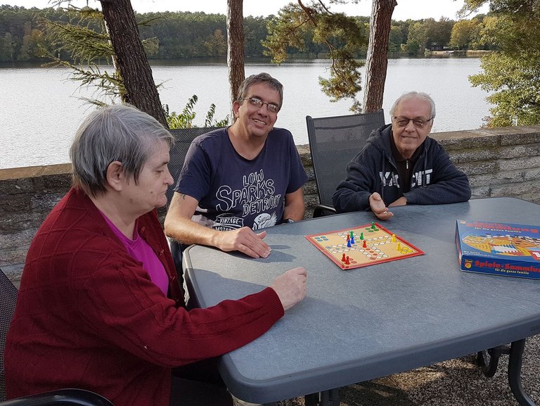 drei Besucher spielen "Mensch ärgere dich nicht" auf der Terasse