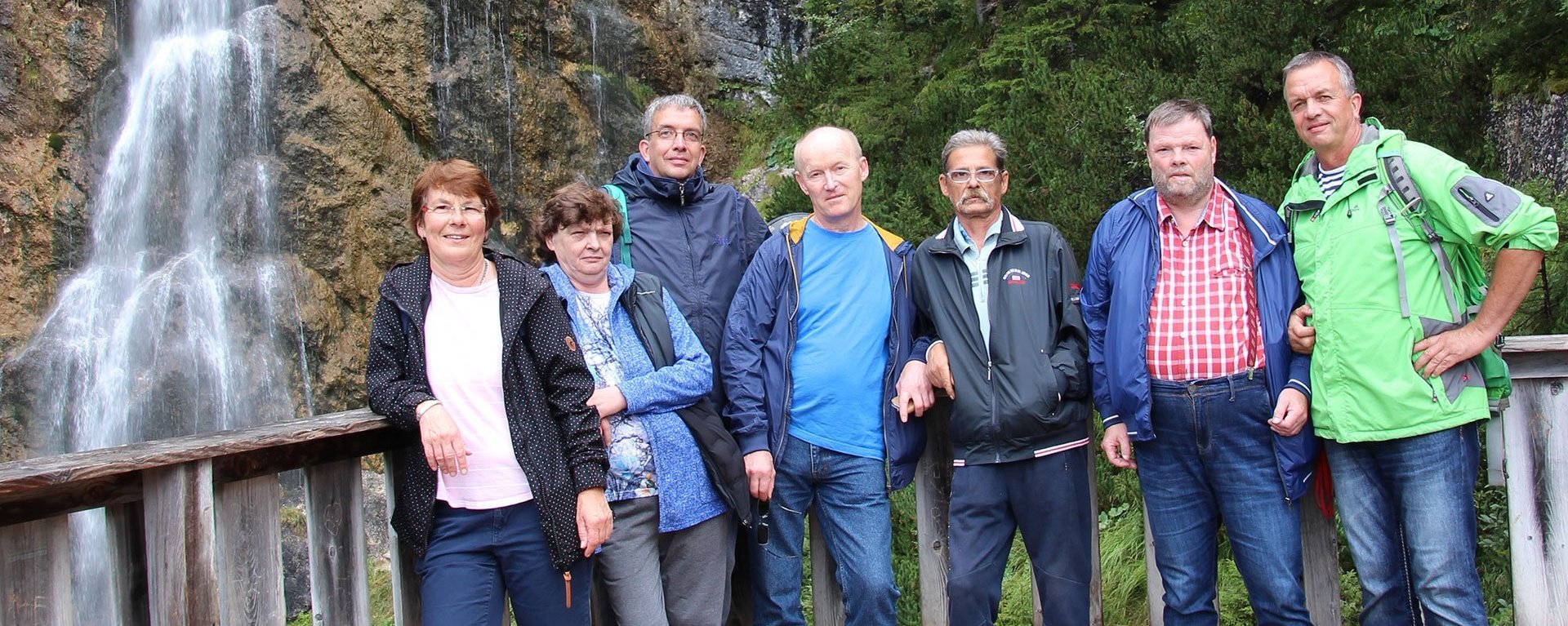 Wanderausflug: Eine Gruppe Frauen und Männer lehnen an einem Geländer - im Hintergrund ein Wasserfall